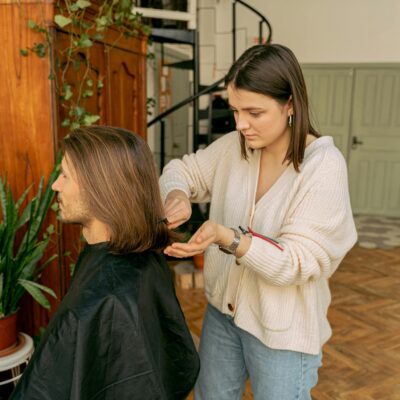 A woman stylist trims a man's hair in a warmly decorated room, showcasing an indoor salon vibe.