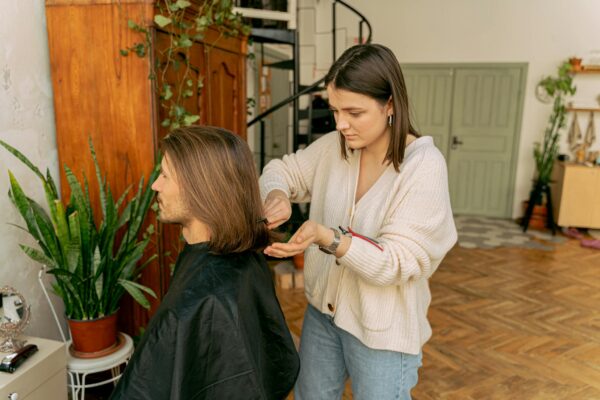 A woman stylist trims a man's hair in a warmly decorated room, showcasing an indoor salon vibe.