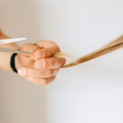 Detailed close-up of a hand holding hair while cutting with scissors against a white background.