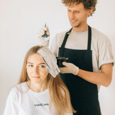 Hairdresser applying color to woman in salon, enhancing beauty with professional care.