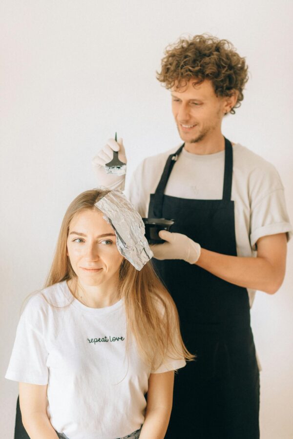 Hairdresser applying color to woman in salon, enhancing beauty with professional care.